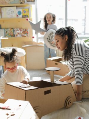 Children and adult engaging in creative play with cardboard toys indoors, fostering imagination.